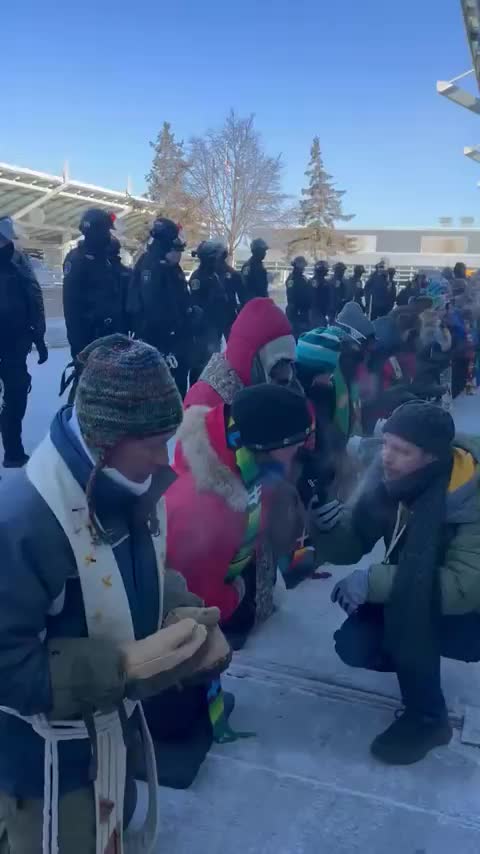 Police line up behind people praying at MSP Airport, for the safety…